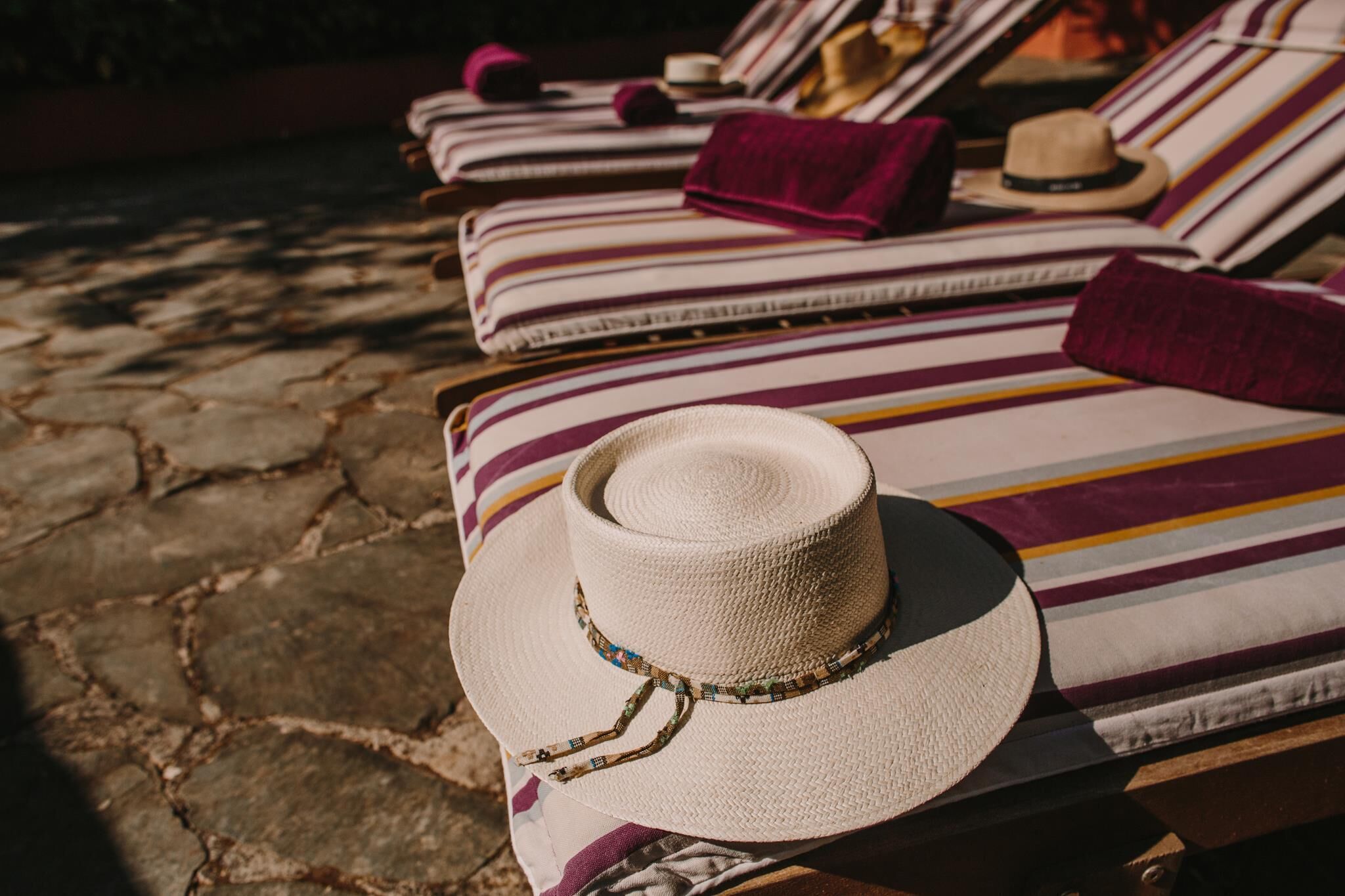 A row of sun loungers with striped cushions and a straw hat placed on one of them.