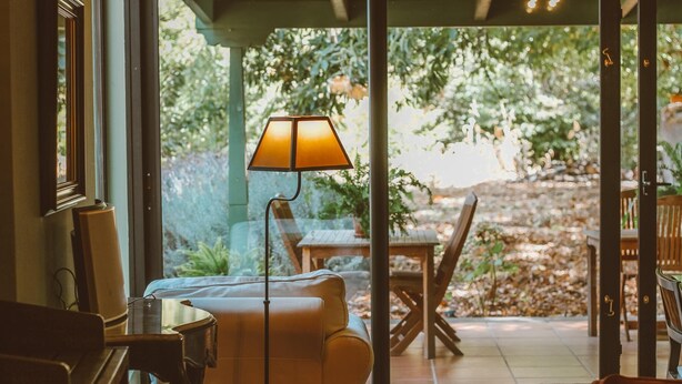 Habitación con sofá, lámpara y vista a un patio exterior con mesa y sillas.