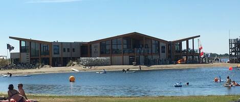 A modern building with large windows and a flat roof, situated by a body of water.
