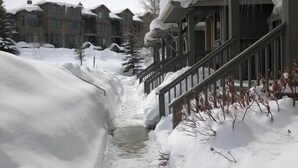 Un sentiero innevato che conduce a un edificio con una scala in legno e un portico coperto.