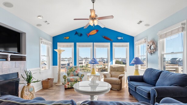 A living room with a blue ceiling, a ceiling fan, a fireplace, a TV, and a view of the outside. - Sandy Bottoms: Oceanside, Pool, Spa, Dogs OK (Nags Head)