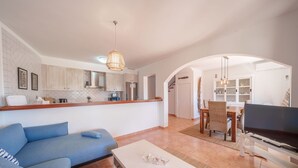 Een moderne woonkamer met een bank, salontafel, televisie en een keuken op de achtergrond.