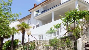 A two-story building with balconies, a stone wall, and a clear blue sky. - Holiday apartment with Interntet access (Rabac)