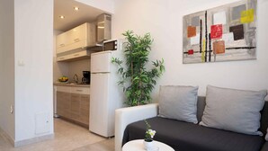 A compact living space with a kitchenette, a sofa with cushions, a potted plant, and a piece of abstract art on the wall. - Holiday apartment with Interntet access (Rabac)