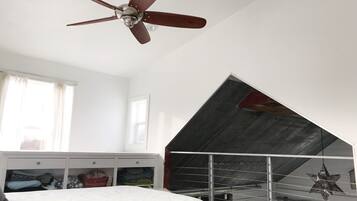 Un dormitori amb un llit, un ventilador de sostre, una finestra amb cortines, un armari blanc i un sostre inclinat.