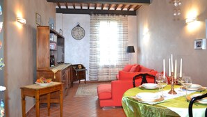 Un comedor con una mesa dispuesta para cuatro personas, un sofá rojo, un armario de madera y un reloj en la pared.