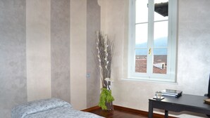 Una habitación con cama, escritorio, silla, ventana y una planta decorativa.