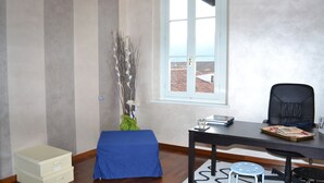 Una habitación con escritorio, silla, ventana, planta y un taburete pequeño.