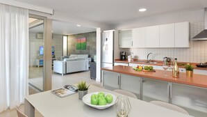 A modern kitchen with a dining area, featuring a white table with a bowl of green apples, a wine glass, and a candle. - Par 4 Rental 9 Salobre by VillaGranCanaria (Maspalomas)