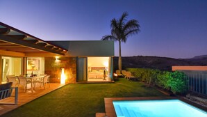 A modern house with a pool, a patio with chairs, and a well-lit interior. - Par 4 Rental 9 Salobre by VillaGranCanaria (Maspalomas)