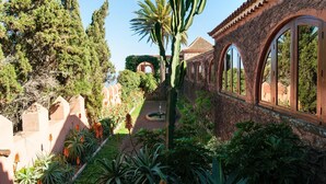 Ein Garten mit Kakteen, Palmen und einem Weg, der zu einem Gebäude mit Bogenfenstern führt.
