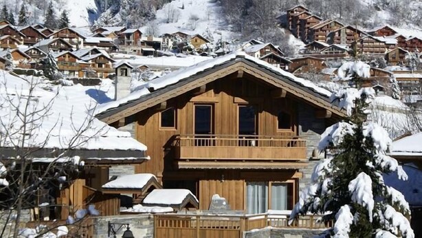 Eine Holzhütte mit Balkon, umgeben von schneebedeckten Häusern in einer Berglandschaft.