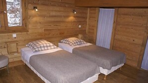 Ein Zimmer in einer Holzhütte mit zwei Betten, jedes mit einem karierten Kissen und einer grauen Decke.