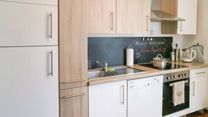 A modern kitchen with white cabinets, a blackboard with chalk writing, a sink, a stove, and a kettle. - 2 bedroom beautiful apartment in Barth (Barth)