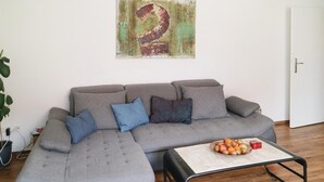A living room with a grey sectional sofa, a coffee table with fruits, and a wall with a large number '2'. - 2 bedroom beautiful apartment in Barth (Barth)