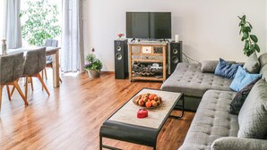 A living room with a grey sofa, a wooden coffee table with fruit, a TV, and a speaker system. - 2 bedroom beautiful apartment in Barth (Barth)