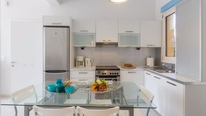 A modern kitchen with white cabinets, a stainless steel refrigerator, a coffee maker, and a glass dining table with chairs. - Calliope Corfu apt - Lovely apartment with garden in Garitsa Bay (Corfu)