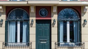 A two-story building with a green door, arched windows, and a balcony with a wrought iron railing. - Calliope Corfu apt - Lovely apartment with garden in Garitsa Bay (Corfu)