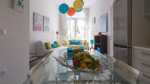 A modern kitchen with a glass dining table, a refrigerator, and a sofa in the background. - Calliope Corfu apt - Lovely apartment with garden in Garitsa Bay (Corfu)