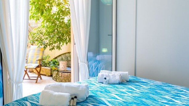 A bedroom with a bed, white towels, and a view of an outdoor area with a tree and a chair. - Calliope Corfu apt - Lovely apartment with garden in Garitsa Bay (Corfu)