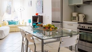 A modern kitchen with a glass dining table, white chairs, a refrigerator, and a coffee maker. - Calliope Corfu apt - Lovely apartment with garden in Garitsa Bay (Corfu)