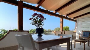 An outdoor patio with a table and chairs, a potted plant, and a view of the landscape. - 1 - House by the sea with pool near Cefalù (Campofelice di Roccella)