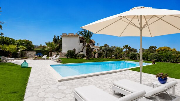 A swimming pool with lounge chairs and an umbrella, surrounded by a well-maintained lawn and a stone pathway. - 1 - House by the sea with pool near Cefalù (Campofelice di Roccella)