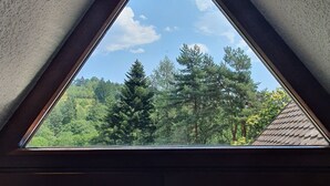 Una finestra triangolare con vista su una foresta e un edificio con tetto in tegole.