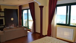Un dormitorio con cama, sofá, un ventanal con vistas al mar y un radiador.