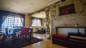 Amplia sala de estar con chimenea de piedra, comedor con mesa y sillas, y un rincón de descanso acogedor con un banco rojo.