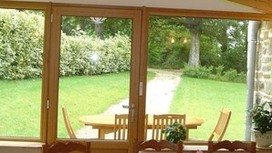 Una habitación con techo de madera, ventanas amplias, una mesa con sillas y una cama con colcha amarilla.