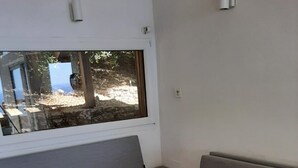 Moderni olohuone, jossa on harmaa sohva, musta sohvapöytä ja suuri ikkuna, josta avautuu näkymä ulos.