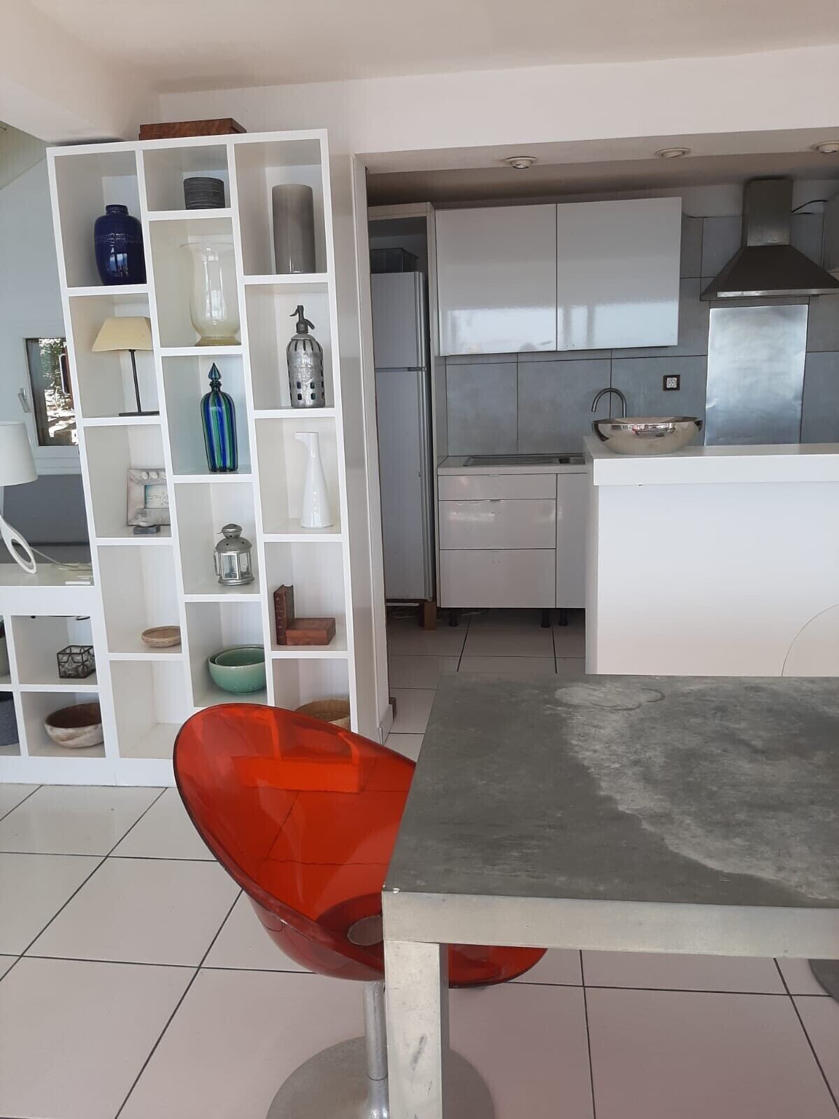 Une cuisine moderne avec des armoires blanches, une hotte de cuisinière en acier inoxydable et un coin repas comprenant une chaise rouge et une table.