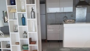 Moderni keittiö, jossa on valkoiset kaapit, ruostumattomasta teräksestä valmistettu liesituuletin sekä ruokailutila, jossa on punainen tuoli ja pöytä.