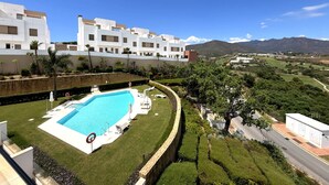 Un hotel moderno con piscina, abundante vegetación y montañas al fondo.