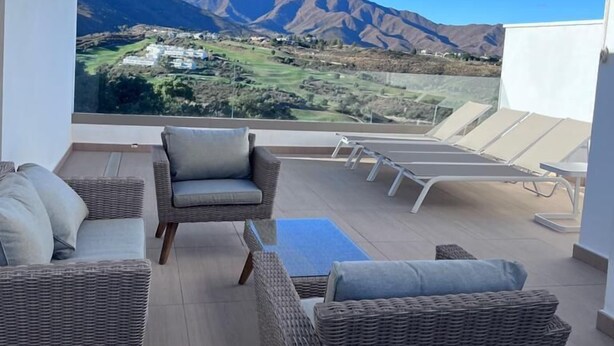 Una terraza con mobiliario de mimbre, vistas a montañas y un cielo despejado.