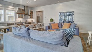 A modern kitchen with white cabinetry, a dining area with a table and chairs, and a living room with a sofa and cushions. - Cinnamon Shore Home Near Beach w/ Access to Resort-Like Amenities! (Port Aransas)