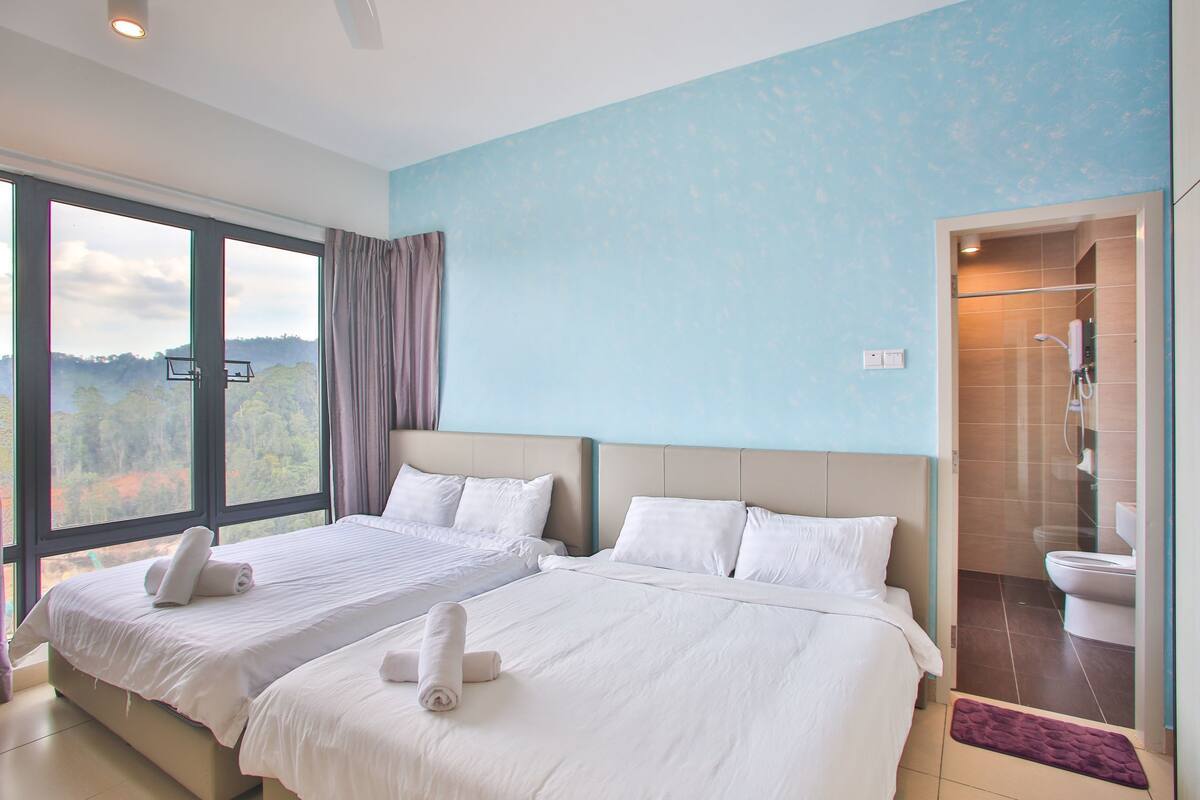 A hotel room with two beds, a large window with a view of the outdoors, and a separate bathroom with a shower and toilet.