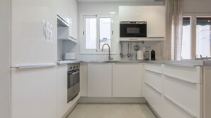 A modern kitchen with white cabinets, a built-in oven, a microwave, and a window with a view. - Discover Sitges, steps from the beach. 3 BRM + 2 BATH (Sitges)
