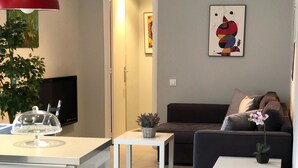 A modern living room with a white sofa, a small coffee table, and a dining area with a white table and chairs. - Discover Sitges, steps from the beach. 3 BRM + 2 BATH (Sitges)