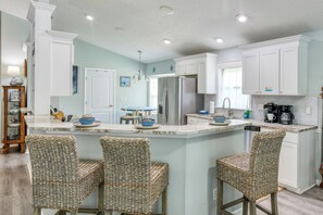 A kitchen with a central island, white cabinetry, and wicker chairs. - Seahorse - Beautiful Beach House with Private Pool & Heated Spa! (Butler Beach)