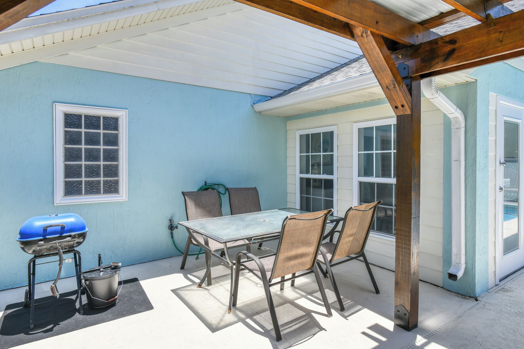 A covered patio with a table and chairs, a grill, and a hose.