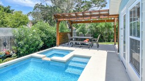 Un jardin avec une piscine, une pergola en bois et une table à manger avec des chaises.
