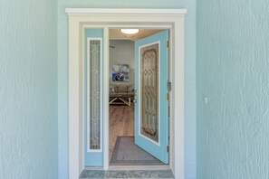 Un couloir mène à une pièce dont la porte est bleue, où l’on trouve un paillasson et un tableau accroché au mur.