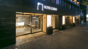 Hotel Kados exteriör präglas av en modern fasad med upplysta skyltar och stora glasfönster.
