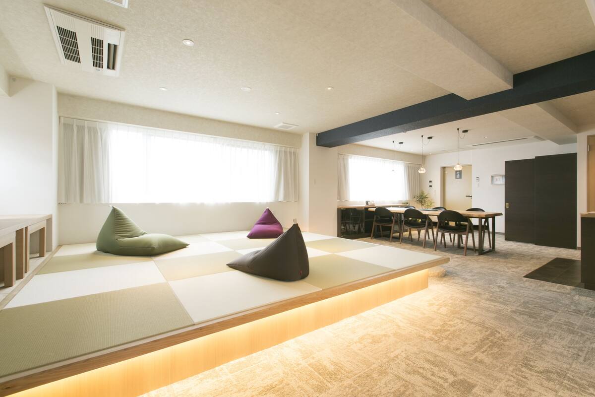 A modern interior with tatami mats, a low wooden platform, and a dining area with chairs and a table.