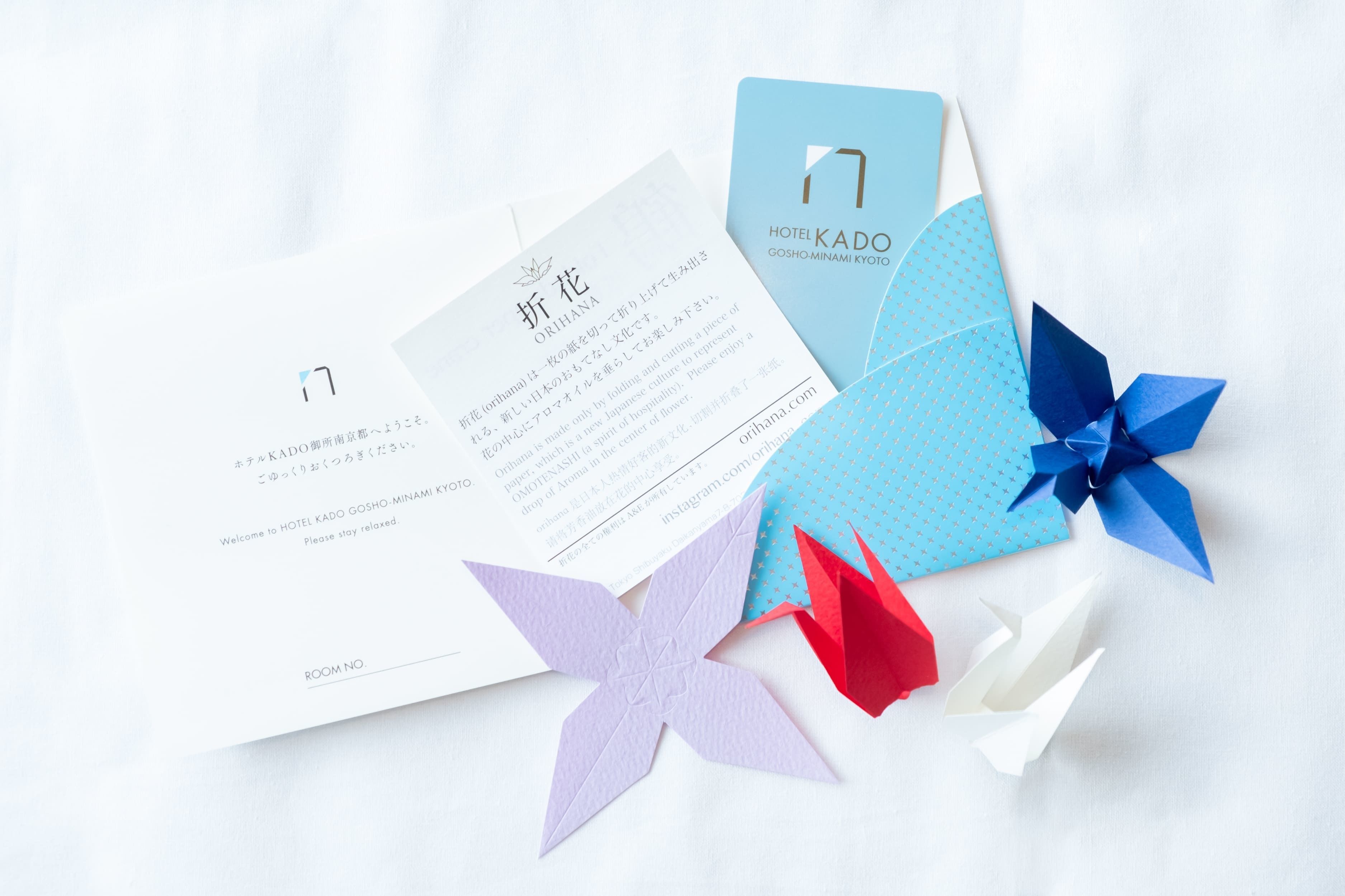 Une chambre d’hôtel avec un couvre-lit blanc, un oreiller à motifs bleus et blancs, et une décoration en origami rouge et blanc.