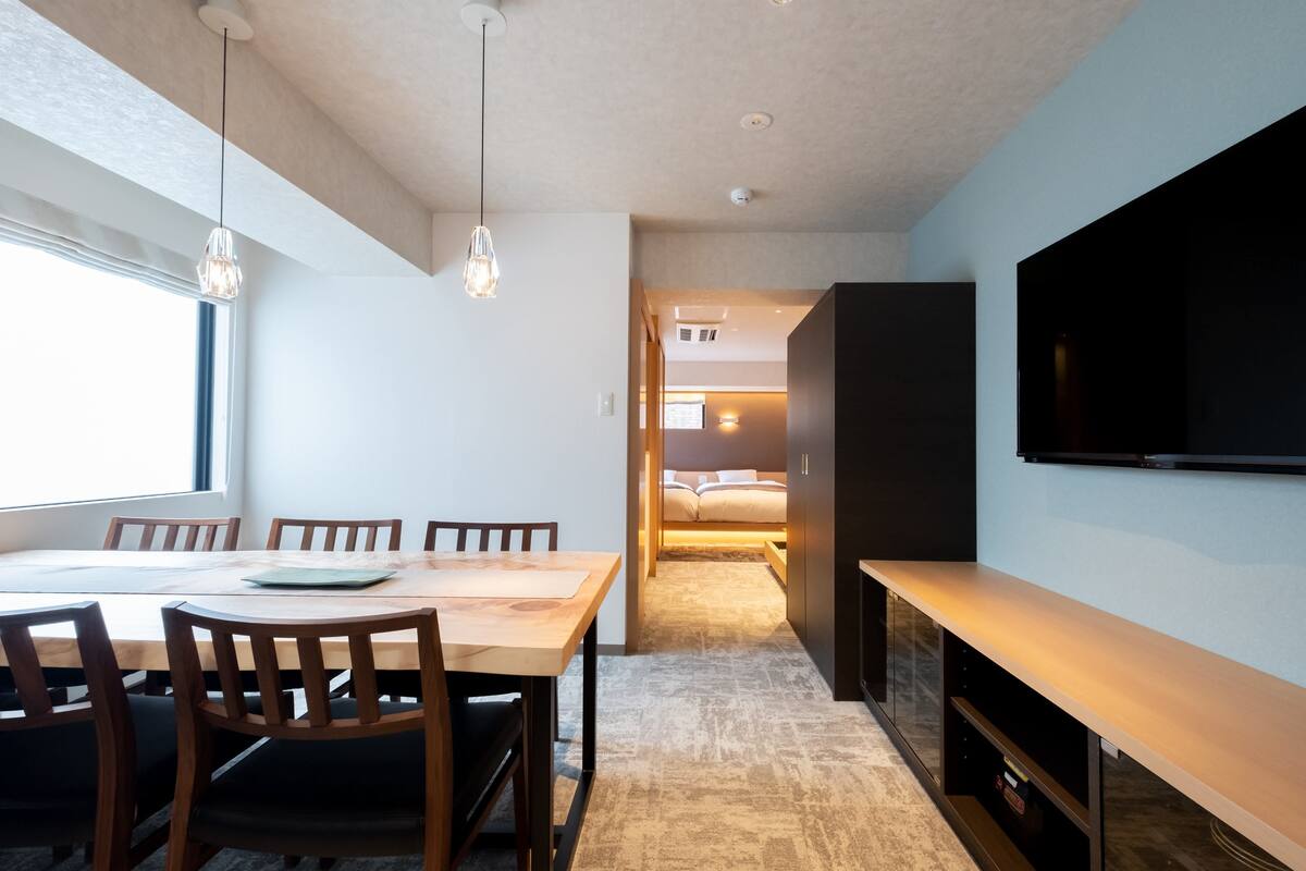 A modern hotel room with a dining area, a large TV, and a cozy bed.
