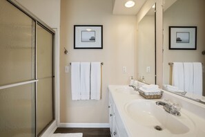 A modern bathroom with a large mirror, two sinks, and a glass shower enclosure.