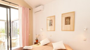 Een hotelkamer met een bed, een nachtkastje, een kamerplant en een schuifdeur die leidt naar een buitenruimte.